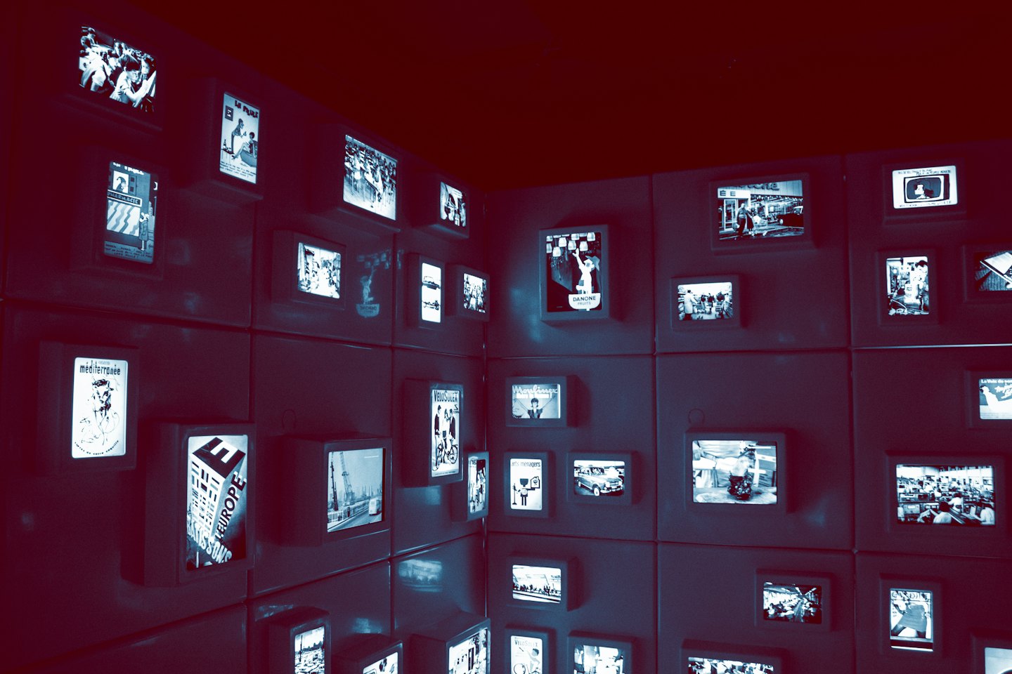 Beleuchtete Bildschirme mit historischen Bildern säumen eine dunkle Museumswand.